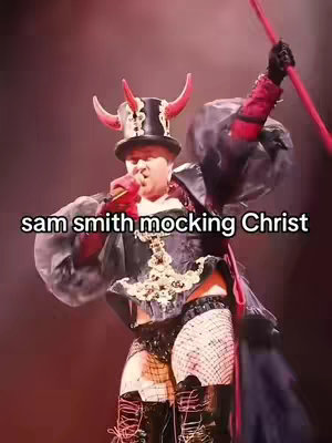The cover image features a person, potentially a performer, on a stage. The person is dressed in an elaborate costume with a black top hat featuring red horns, a black outfit with gold ornamentation, and fishnet stockings. The background appears to be a stage with red and black lighting. Text overlayed reads "sam smith mocking Christ."