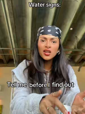 A woman with long dark hair and a black bandana on her head speaks directly to the camera. She's wearing a gray hoodie, and in the background a metal structure as the ceiling.