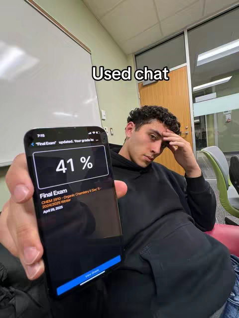 A young man is shown holding a phone displaying a failing exam grade of 41%. He appears dejected, resting his hand on his forehead while sitting in a well-lit room with a whiteboard in the background.