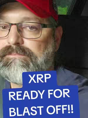 A selfie-style shot featuring a man with glasses and a beard looking directly at the camera. He is wearing a red hat. In the foreground, a blue rectangle displays the text 'XRP READY FOR BLAST OFF!!'.