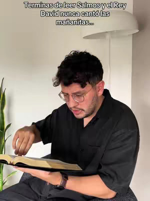 A man is seated, holding an open book, wearing a black shirt and glasses. Text overlayed.