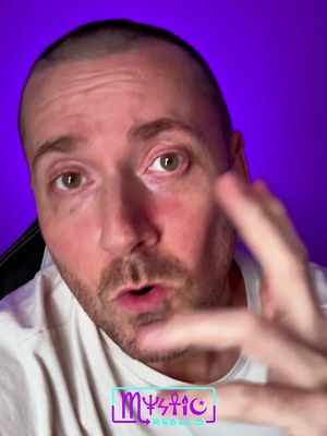 A close-up of a man with short hair, fair skin, and green eyes looking directly at the camera. He's positioned in front of a purple background, and the lower third of the frame includes a teal box with the words "Mystic Rebels" in stylized purple lettering.