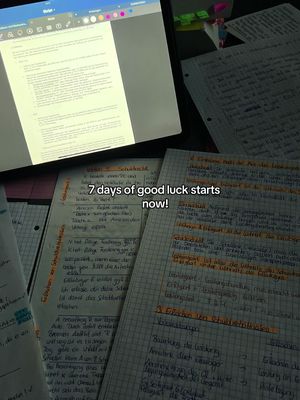 A workspace setup with a tablet displaying notes, surrounded by various handwritten papers. Text overlays are present on the handwritten notes. The lighting is dim, focusing on the task.