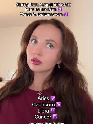 A selfie-style shot of a woman with long, wavy brown hair and a burgundy top. She's looking at the camera with a slight smile, wearing lipstick. Text overlays at the top and bottom provide context: astrological information, including planet positions and zodiac signs.