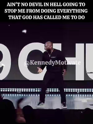The image captures a man on a stage, likely a preacher, gesturing with one arm extended and the other pointing at the audience. Large white letters spell a word in the background, set against a dark backdrop. The man is wearing a dark, collared shirt and black pants, and a subtle glow surrounds him. The stage appears to be set for a motivational or religious talk.