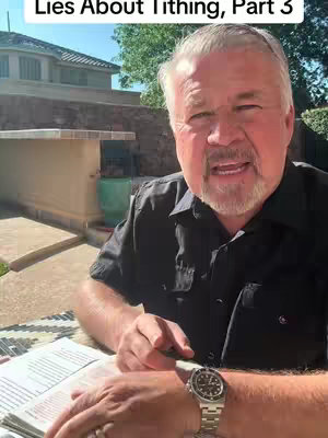 A man of mature age with gray hair and a beard is the central figure, positioned slightly off-center in front of an outdoor backdrop. He is wearing a black button-down shirt, and the lower portion of his hands are visible, one of which holds what appears to be a book. In the corner, there is text overlayed atop a blurred background and a building to which he is looking at. The background is a well-lit outdoor setting.