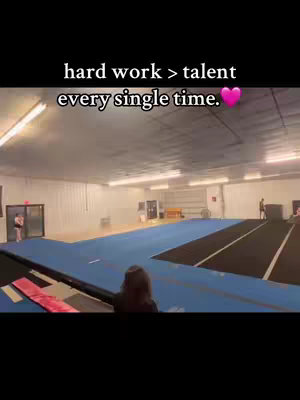 A wide shot of a gymnastic studio with blue and black mats, a person is in the foreground, and text overlays.