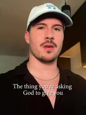 A man with a mustache and a white baseball cap is centered in front of the camera. The background is blurred, suggesting an interior setting. Text overlayed on the bottom part of the image.