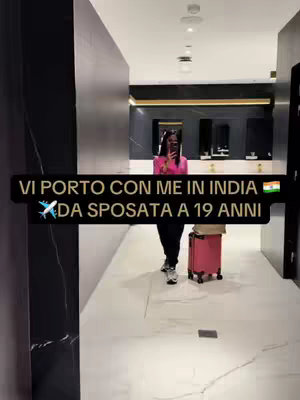 A woman is walking towards the camera in what appears to be an airport terminal, with a pink suitcase. The background is modern and minimalist with dark walls and a bright, white floor.