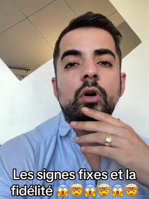 A man with a beard and short dark hair looks directly at the camera, a quizzical expression on his face. He is wearing a light blue button-up shirt and a gold ring. Text at the bottom reads, in French, "Les signes fixes et la fidélité," followed by several emoji faces.