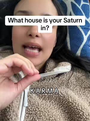 The cover image shows a close-up of a woman's face in a selfie-style shot. She has dark hair and is wearing a beige, textured sweater. A white text bubble overlay at the top reads 'What house is your Saturn in?' At the bottom, the word 'KARMA' is overlaid in white text. The woman's face is centered, with part of her hand holding a light-colored object near her face.