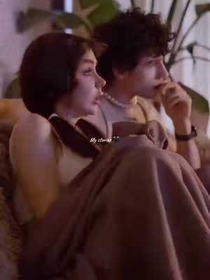 The cover image shows a young couple in a dimly lit setting. They are seated closely together, partially covered by a blanket. The woman is in profile, facing left, with dark hair in a ponytail. The man is also in profile, looking towards the distance, next to the woman. The setting suggests intimacy and closeness.