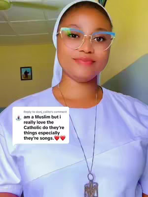 A woman with fair skin wearing glasses and a white head covering is smiling at the camera. The background includes a small framed picture on the left and part of a ceiling.