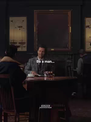 A man in a suit, seated at a table, smiles as he looks down at something, appearing to be either reading or writing behind a table with someone out of focus sitting left, with two people in the background. There is text overlaid on the image.