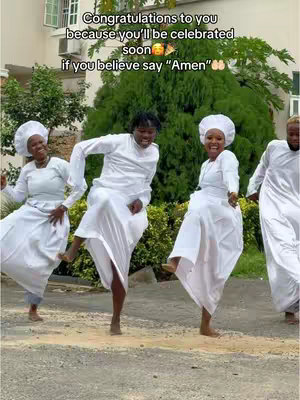 Four individuals dressed in white robes and head coverings are captured mid-dance with expressions of joy. The background includes a building, foliage, and a sidewalk.