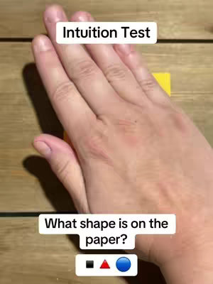 The cover image shows a hand placed over a yellow rectangle on a wooden surface. The hand is positioned centrally. Below this, an overlay presents options: a black square, a red triangle, and a blue circle. Text overlays state 'Intuition Test' at the top, and 'What shape is on the paper?' below the subjects' hand.