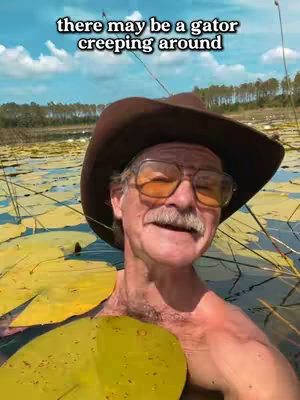 A man in a brown hat and glasses in a pond of lily pads. White text overlays the top of the image.