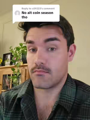 A man with dark hair and a mustache looks at the camera with a neutral expression. He is wearing a green and black plaid shirt. A speech bubble in the top-left corner reads, "No alt coin season tho."