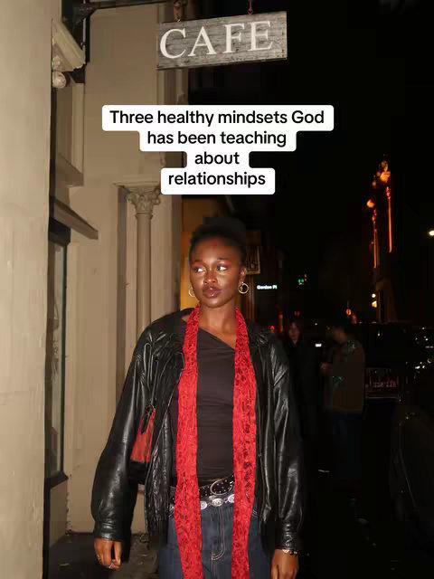 A woman stands in front of a cafe at night. She wears a black leather jacket over a black top, with a red scarf and blue jeans. Text is overlaid at the top of the image.