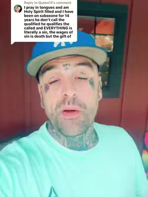 A man with face and neck tattoos, wearing a blue baseball cap and a light green t-shirt, speaks to the camera. A text overlay replicates a comment.