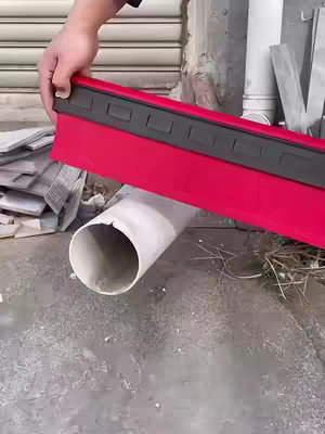A person holds a red and black tool, possibly a contour gauge, over a white pipe and concrete surface. The scene is well-lit, suggesting a construction or DIY setting.