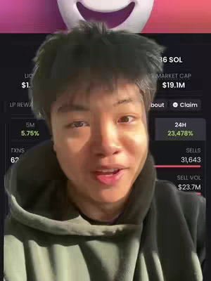 A young man with short, dark hair, wearing a green hoodie, is positioned in front of a screen displaying cryptocurrency data. His facial expression suggests he is speaking or reacting to the content on the screen. Above him is a large, smiling, white face graphic, possibly a branding element.
