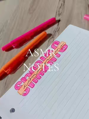 The image displays a close-up of a notebook page with an elaborate title written across it, along with a couple of markers. The title, "ASMR NOTES," is in a playful, bubble-letter style, emphasized by the vibrant pink hue for the outline filling the letters. The word "NOTES" is accented within the shape, and the overall style is bright and playful. Beside the title lies highlighters of contrasting colors.