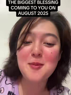 A female face, centered and filling most of the frame. She has short, dark hair, parted on one side, framing her face. A banner with white text sits across the top, and she appears to be smiling slightly with her mouth closed. Her cheeks are flushed with pink.