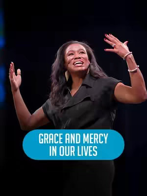 A woman with long dark hair and a black top stands on a stage with her arms raised, looking upwards with a smile. A teal-colored graphic with white text at the bottom of the image adds messaging to it.