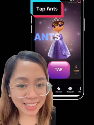 A woman with glasses is smiling at the camera in front of a phone displaying a game called "Tap Ants". The phone screen shows a cartoon ant wearing a crown and a purple dress, with the word "ANTS" in large letters. A banner at the top says "Tap Ants".