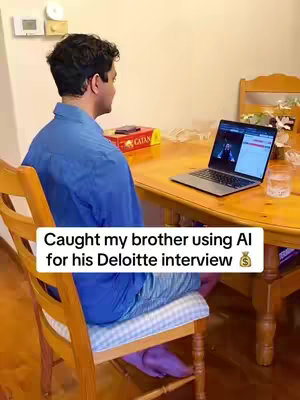 A person is sitting at a wooden table with a laptop open, appearing to be in an interview. The foreground shows their back, seated on a chair, while a text overlay states content about the AI tool assisting in the video interview.