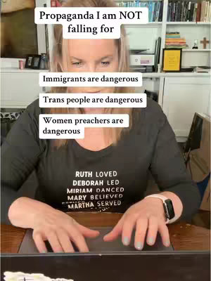 A woman is shown in a close-up shot, seated in front of a desk with a laptop, with shelves and books in the background. Above her head are text overlays in white boxes containing statements such as “Propaganda I am NOT falling for” and other statements. The woman has blonde hair and is wearing a dark long-sleeved shirt.