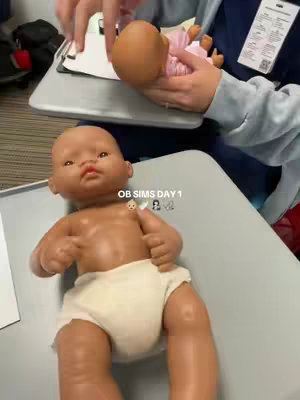 The cover image shows a baby doll in a diaper lying on a gray surface. The doll is facing the viewer with arms outstretched. An additional doll, dressed in a pink outfit is being held off to the side by a person. The text 'OB SIMS DAY 1' is overlaid on the image..