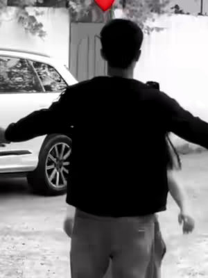 A black and white image shows a man from the back, his arms outstretched, embracing another person out of the frame as if giving them a hug. A car is parked by the side. Above the man is a red heart.