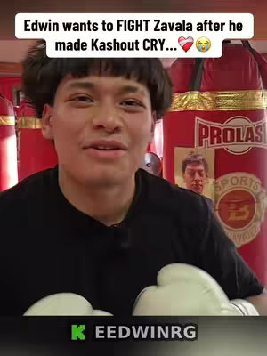 A selfie-style shot of a young man in a black t-shirt wearing white boxing gloves, looking at the camera, with text in a white banner overlayed on top. He is positioned in front of a red punching bag and other red and yellow gym equipment. Behind him is another person. The background features a boxing gym environment.
