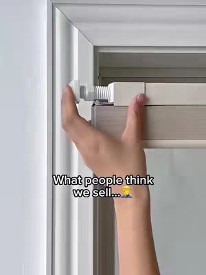 A hand is shown holding a white bracket and turning what appears to be a screw attached to a white door frame, white blinds are behind it. Text in the lower third reads, "What people think we sell..." with a person emoji with a yellow face
