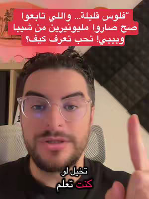 A man with glasses is speaking to the camera, with overlaid text in Arabic. He is gesturing with a raised index finger. Behind him is a dark wall and some studio equipment.