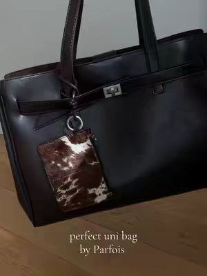 A close-up shot of a black Parfois handbag against a neutral background. A small leather tag is attached to the handle. Text overlaid at the bottom reads 'perfect uni bag by Parfois'.