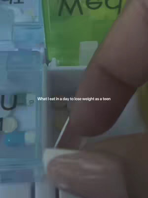 An image shows a person's hand opening a compartment of a pill organizer, revealing pills and the text overlay: "What I eat in a day to lose weight as a teen". The background includes other compartments.