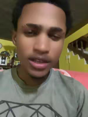 The cover image shows a young man in a medium shot, with a slightly upward camera angle. He is positioned in the center, with a green t-shirt. The background appears to be a domestic setting, with yellow walls and a glimpse of a staircase to the right. The lighting is natural, and the man has dark hair and is looking towards the camera.