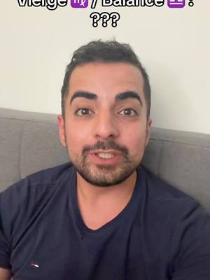 A man with short dark hair and a trimmed beard is centered in the frame, against a nondescript beige wall and a gray sofa. He seems to be filming from a low angle. Above his head is the text overlay. He is wearing a dark blue t-shirt and looking directly at the camera with an open mouth, suggesting he is speaking. The lighting is bright and even.