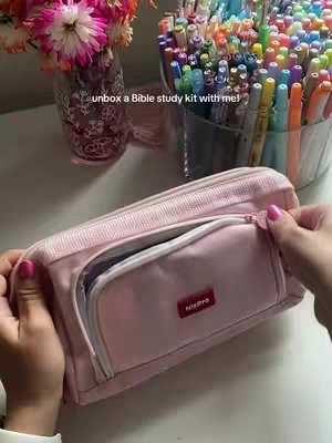 The cover image shows a workspace, with a pink pencil case in the foreground. The zipper is open, revealing the inside. In the background, there are several colorful pens and markers in a container and a vase with flowers.