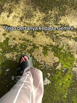 The image shows a foot in dark sandals and white pants on a surface covered with moss and small plants. Text overlay at the top in white font reads, 'Virgo bertanya kepada Gemini' (Virgo asks Gemini).
