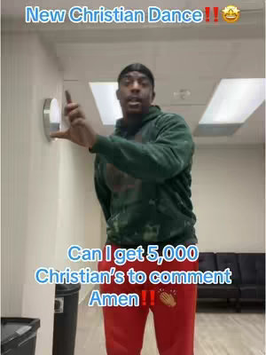 A man in a green hoodie and red pants stands inside a building with a wall-mounted light and black couches in the background. The man points with his right index finger towards the left while speaking. Text overlay is applied at the top and bottom of the image.