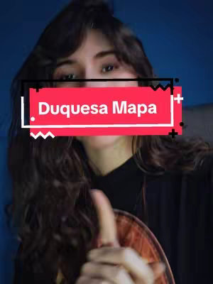A woman with long, wavy dark hair pointing her right index finger upwards. She is facing forward, looking slightly upwards and smiling. A rectangular overlay with the text "Duquesa Mapa" in white letters is on her upper chest and around her face. The background is blue.