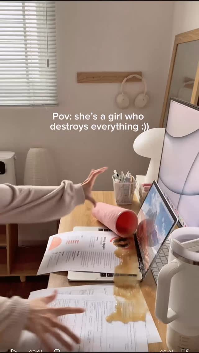 A POV shot shows a cluttered desk with a computer, papers, and a spilled drink. The creator's hand reaches out as if knocking over a cup of liquid.