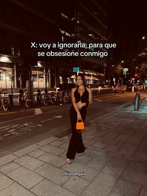 The image shows a woman standing on a city sidewalk at night. She's wearing a black outfit and holding an orange purse. Text overlays appear. The street is lit by streetlights and buildings. Background features parked bicycles.