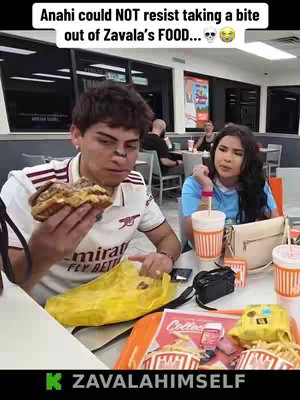 A man is shown with an exaggerated expression as though he's been caught off guard while half-eating a burger, and to his right is a woman in a more neutral expression. They are in a restaurant setting.