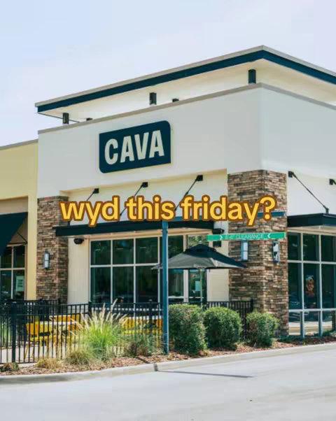 An exterior shot of a CAVA restaurant. The building is cream-colored with a dark blue sign that reads CAVA. The phrase "wyd this friday?" is overlaid on the image in a yellow, bubble font. There is also a street sign that says "Entrance".