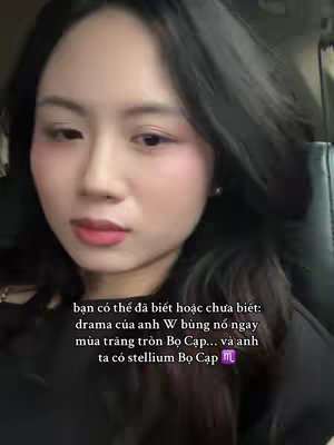 A selfie-style shot featuring a woman's upper body. She is indoors, and her dark hair frames her face, which is angled slightly to the side. She wears light makeup, featuring blush and lipstick. Text overlay is at the bottom, partially obscuring the image.